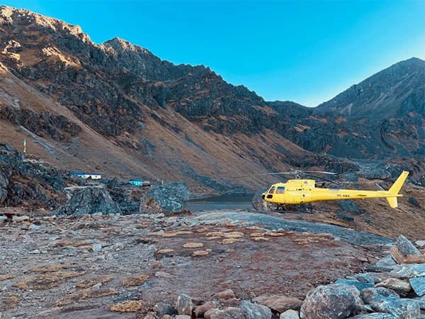 A helicopter flying over Gosainkunda Lake with the surrounding snow-capped peaks and pristine blue waters below.